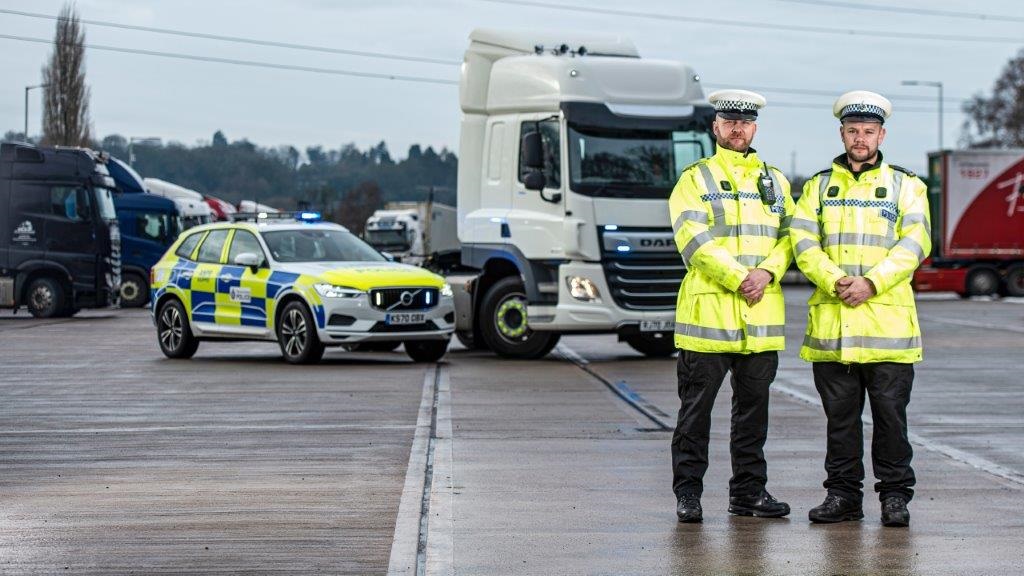 Two officers standing in front of a HGV and car