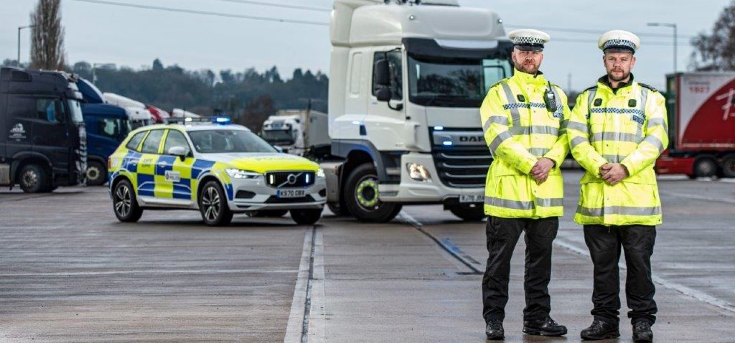 Two officers standing in front of a HGV and car